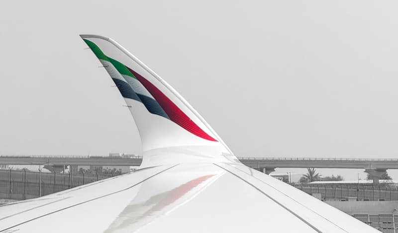 An Emirates aircraft winglet in the airline's red, green and black livery, seen from the cabin window